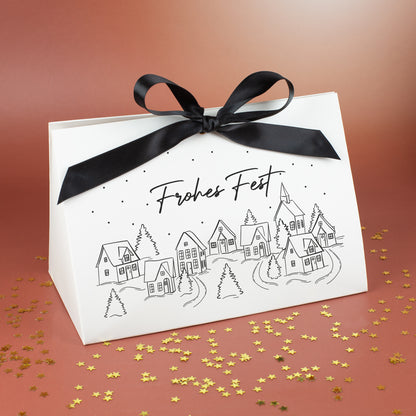 Große Geschenktasche mit Winterdorf-Motiv und Aufschrift „Frohes Fest“, vor warmem Hintergrund und goldenen Sternstreu-Elementen präsentiert.