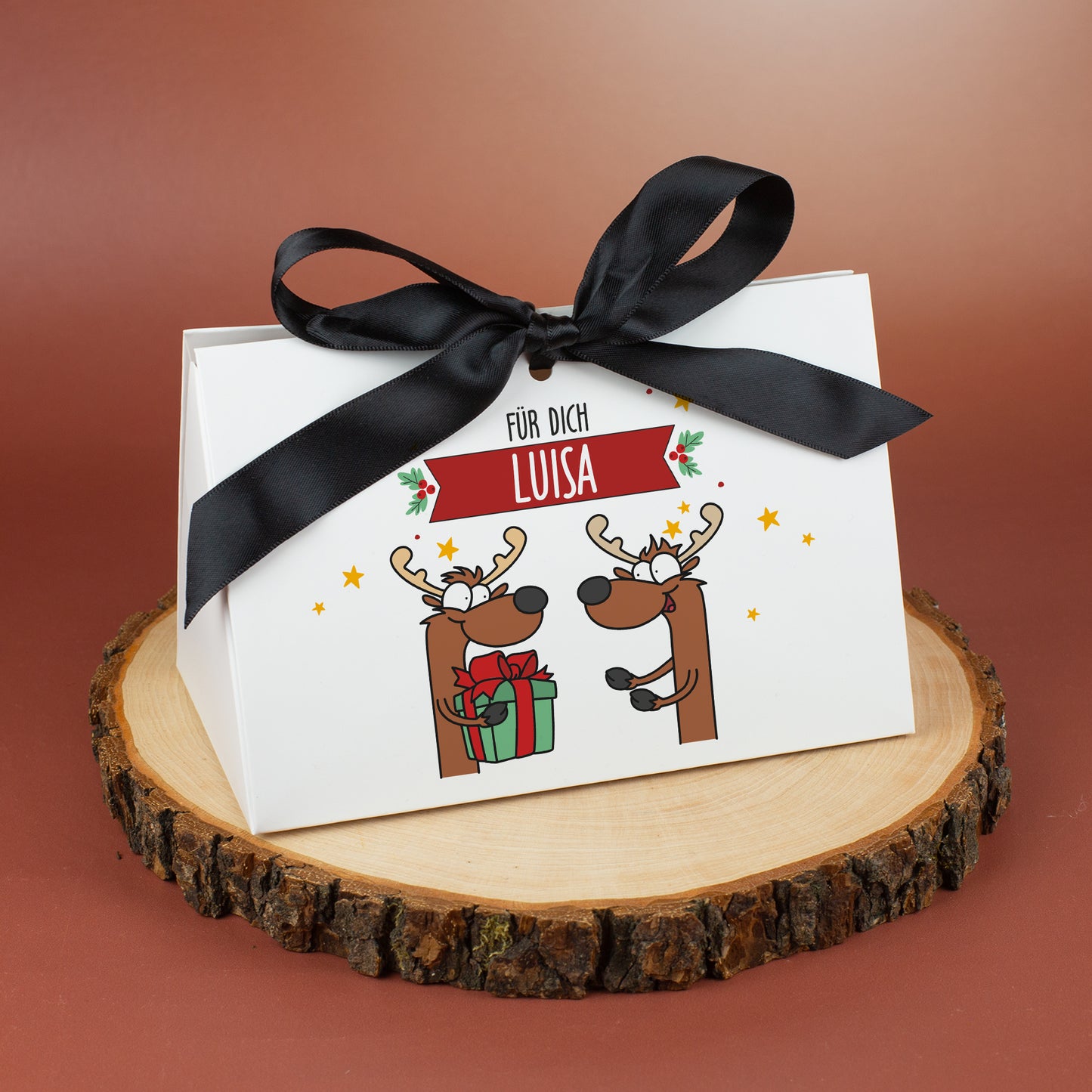 Mittlere Geschenktasche mit Rentiermotiv und Name „Luisa“, auf einer Holzscheibe vor rötlichem Hintergrund präsentiert.