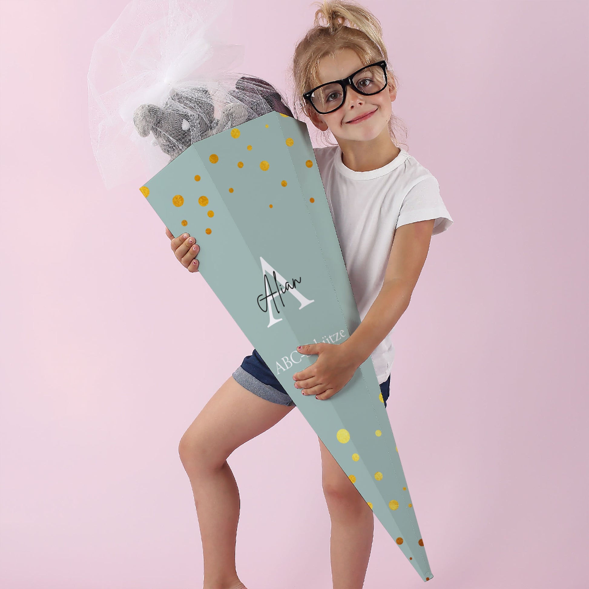Mädchen mit mintgrüner Schultüte und weißer Initiale, fröhlich lachend