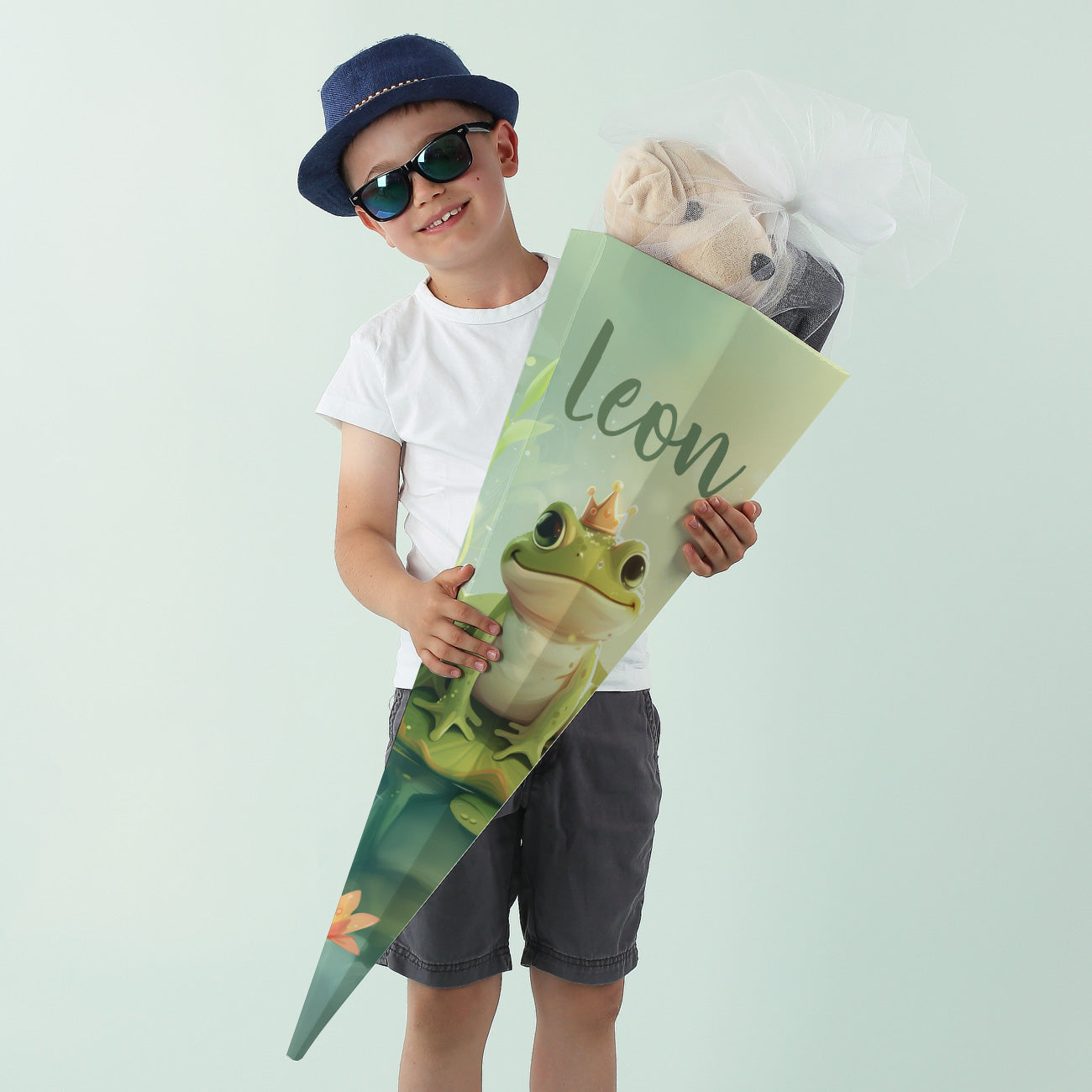 Junge mit Sonnenbrille hält eine personalisierte Froschkönig-Schultüte mit dem Namen "Leon"