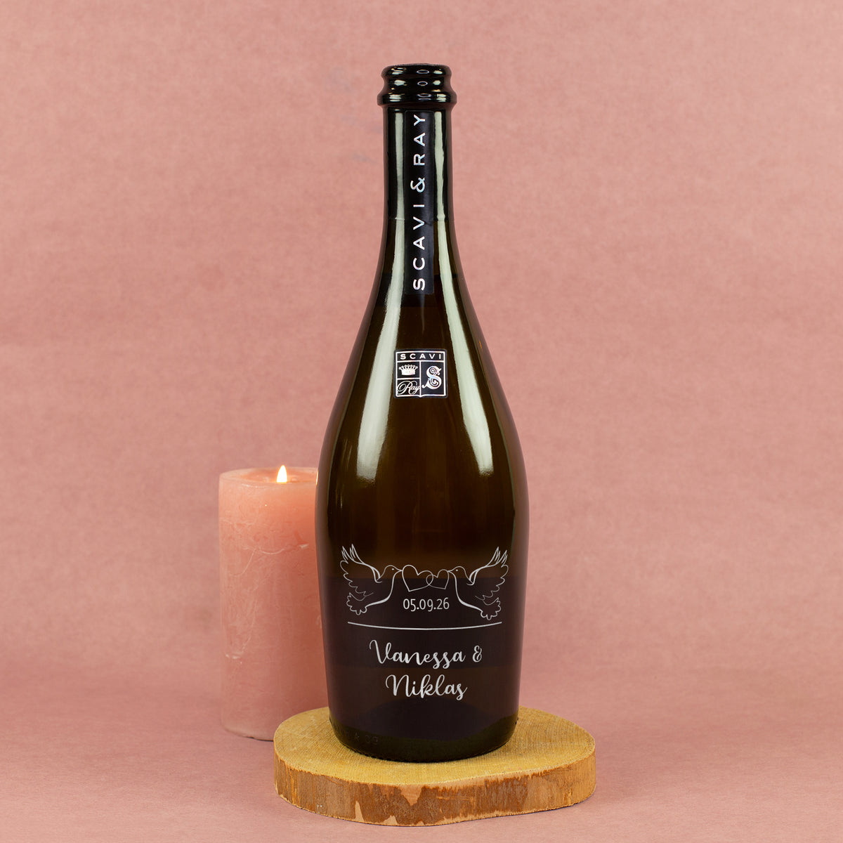 Personalisierte Prosecco-Flasche zur Hochzeit mit Tauben, Herzen, Datum und Namen Vanessa & Niklas neben Kerze