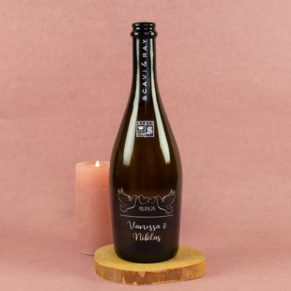 Personalisierte Prosecco-Flasche zur Hochzeit mit Tauben, Herzen, Datum und Namen Vanessa & Niklas neben Kerze