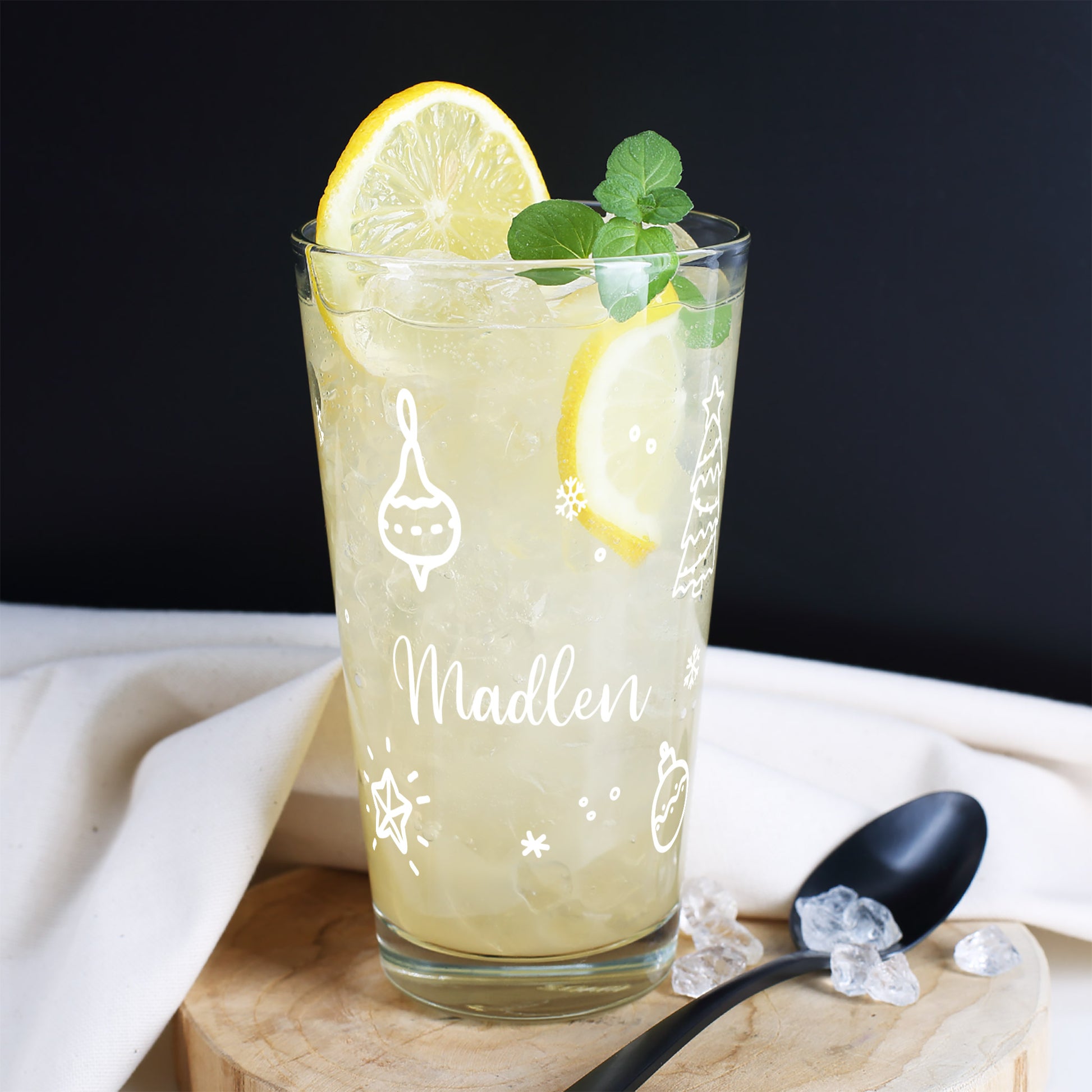Weihnachtliches Trinkglas mit Ornament-Motiv, Name Madlen, befüllt mit Zitronengetränk und Eis, dekoriert mit Minze.