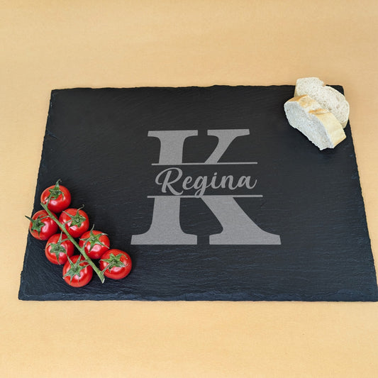 Schieferplatte mit Gravur „Regina“ und Initiale „K“, dekoriert mit Tomatenrispe und Brotscheiben auf beigem Hintergrund