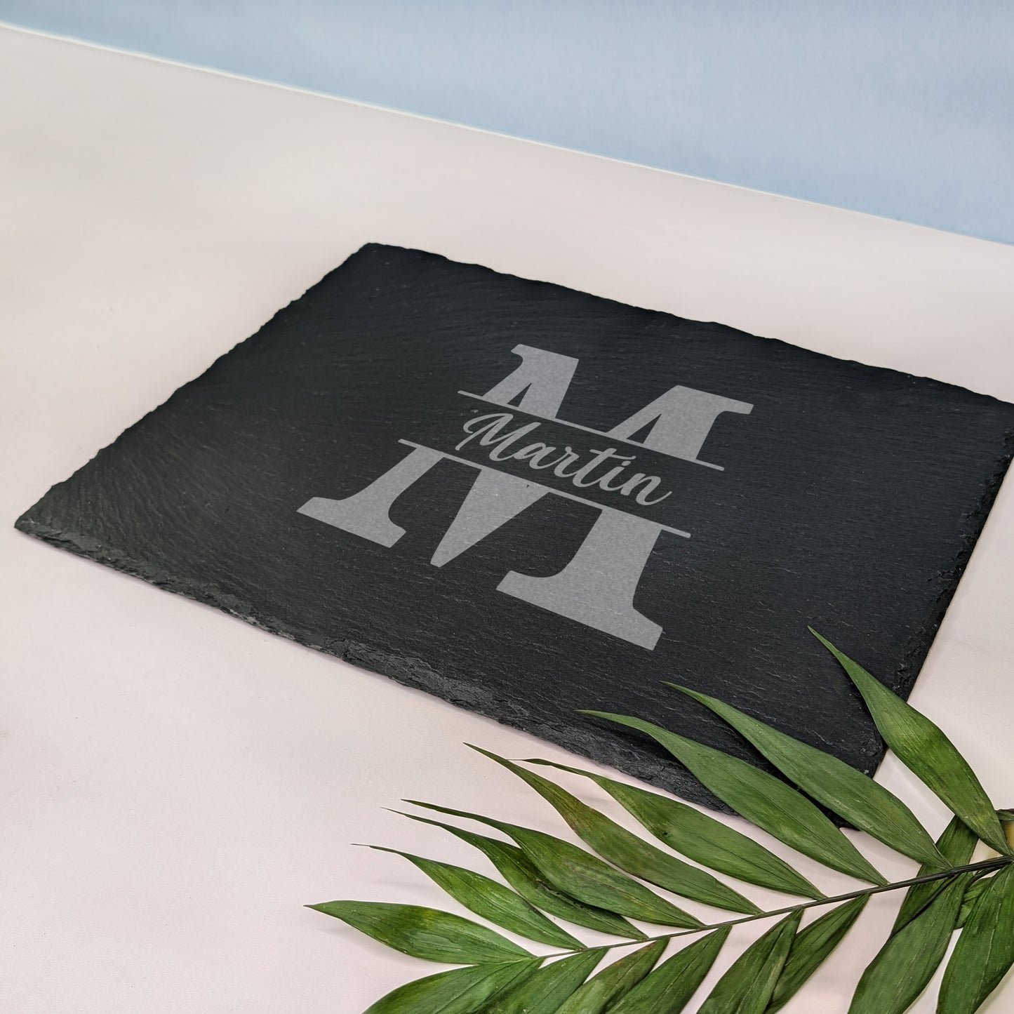 Schieferplatte mit Gravur „Martin“ und Initiale „M“, auf hellem Untergrund mit grünem Blattzweig – seitliche Perspektive