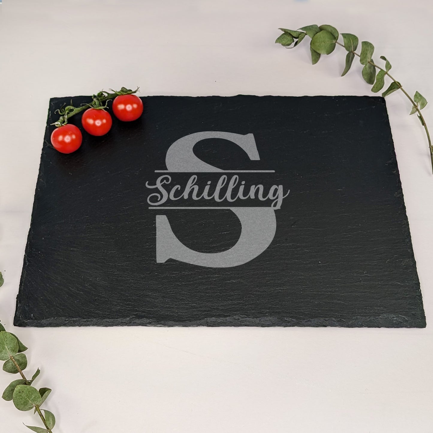 Schieferplatte mit Gravur „Schilling“ und Initiale „S“, dekoriert mit Tomaten und Eukalyptus – auf hellem Hintergrund