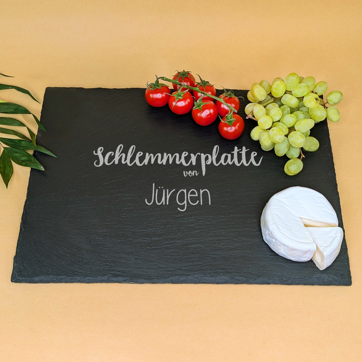Schieferplatte mit Gravur „Schlemmerplatte von Jürgen“, dekoriert mit Käse, Tomaten, Trauben und Blättern