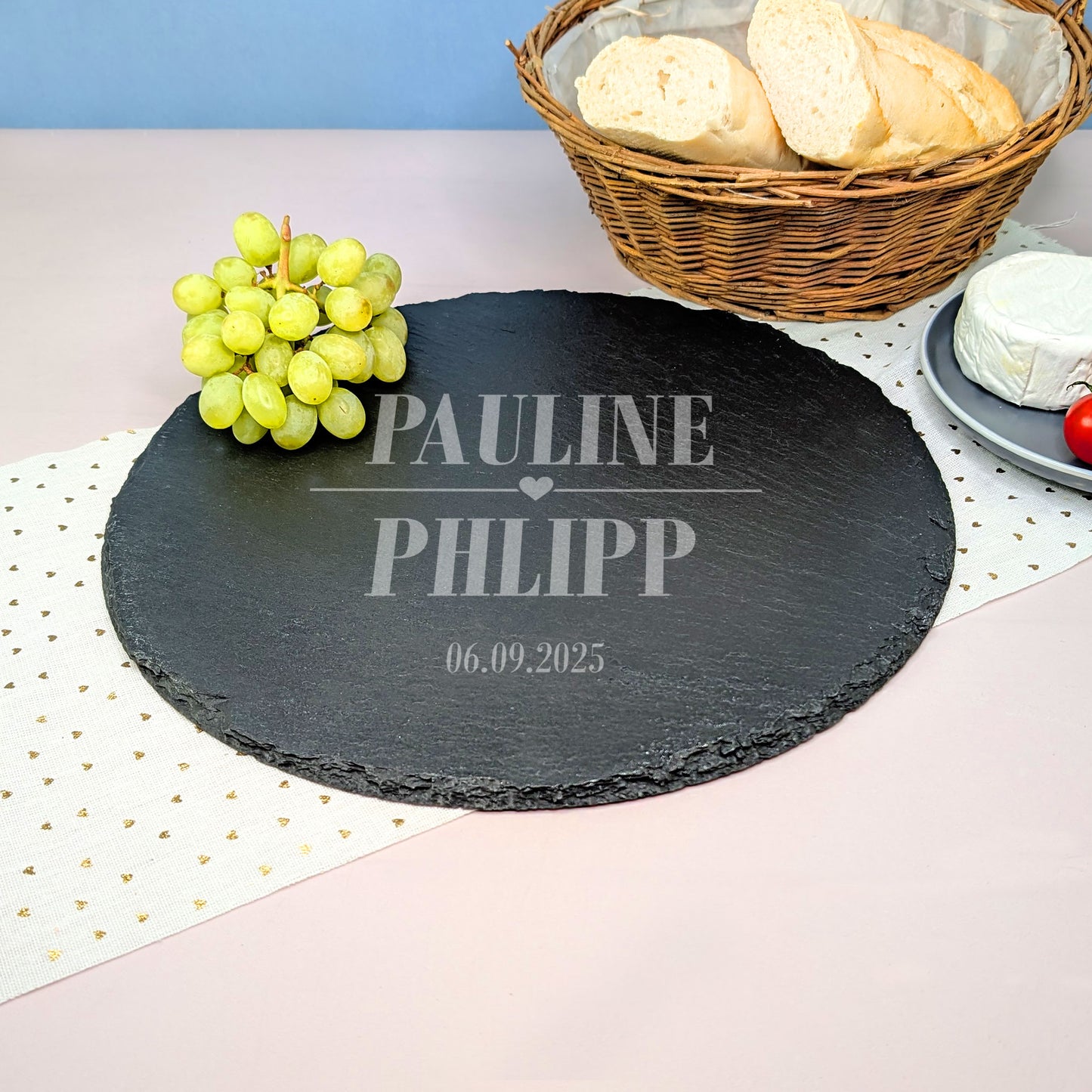 Personalisierte Schieferplatte mit Herzmotiv Gravur, zwei Namen und Datum, dekoriert mit Weintrauben, Käse, Tomaten und Baguette.