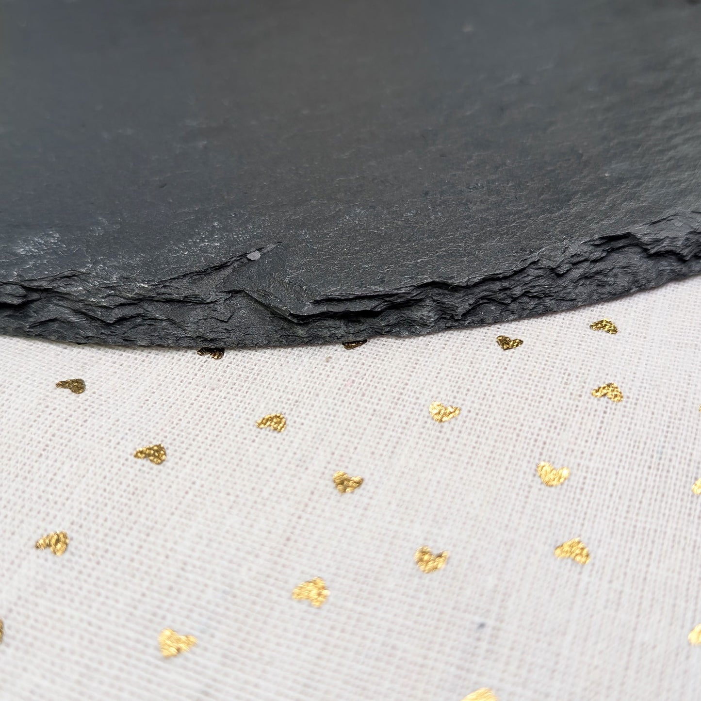 Nahaufnahme der natürlichen Bruchkante der Schieferplatte auf weißem Tuch mit Goldpunkten