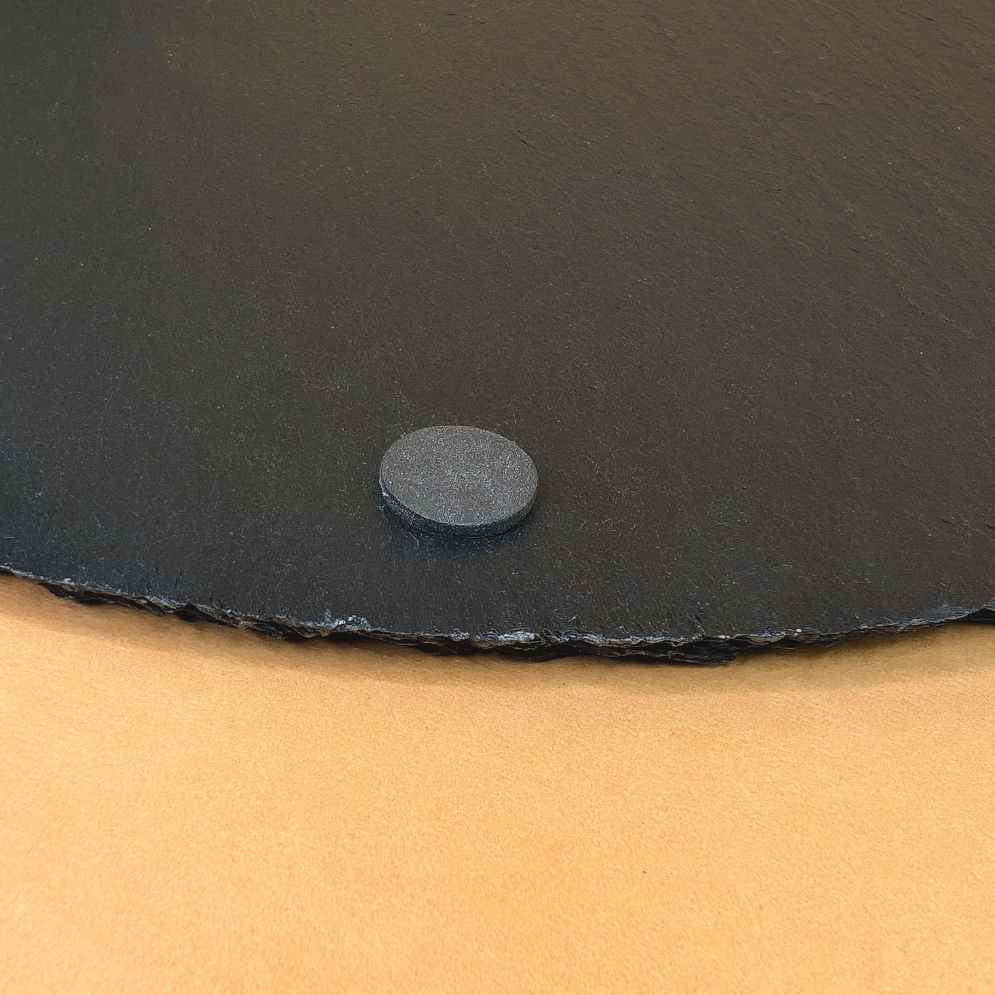 Detailaufnahme eines Gummifußes an der Unterseite der Schieferplatte auf gelbem Hintergrund