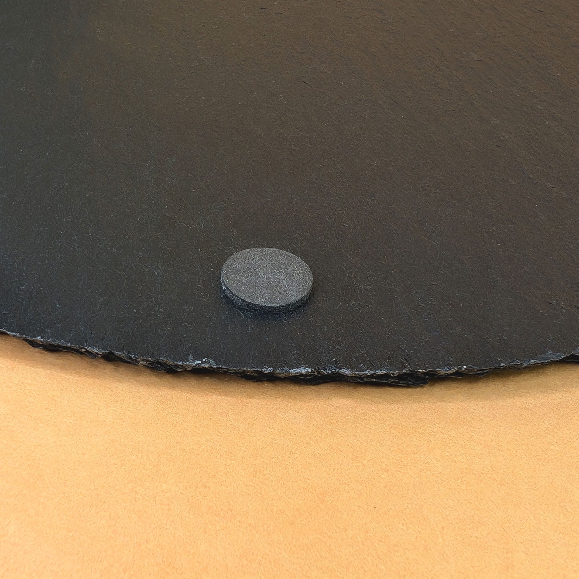 Detailaufnahme eines Gummifußes an der Unterseite der Schieferplatte auf gelbem Hintergrund