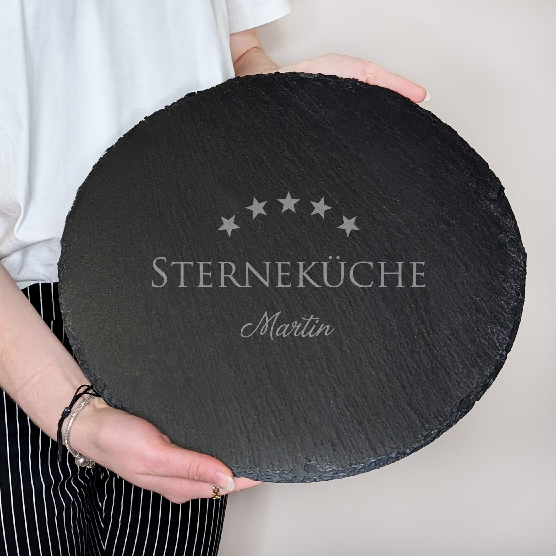 Runde Schieferplatte mit Gravur „Sterneküche“ und Name Martin, von zwei Händen gehalten