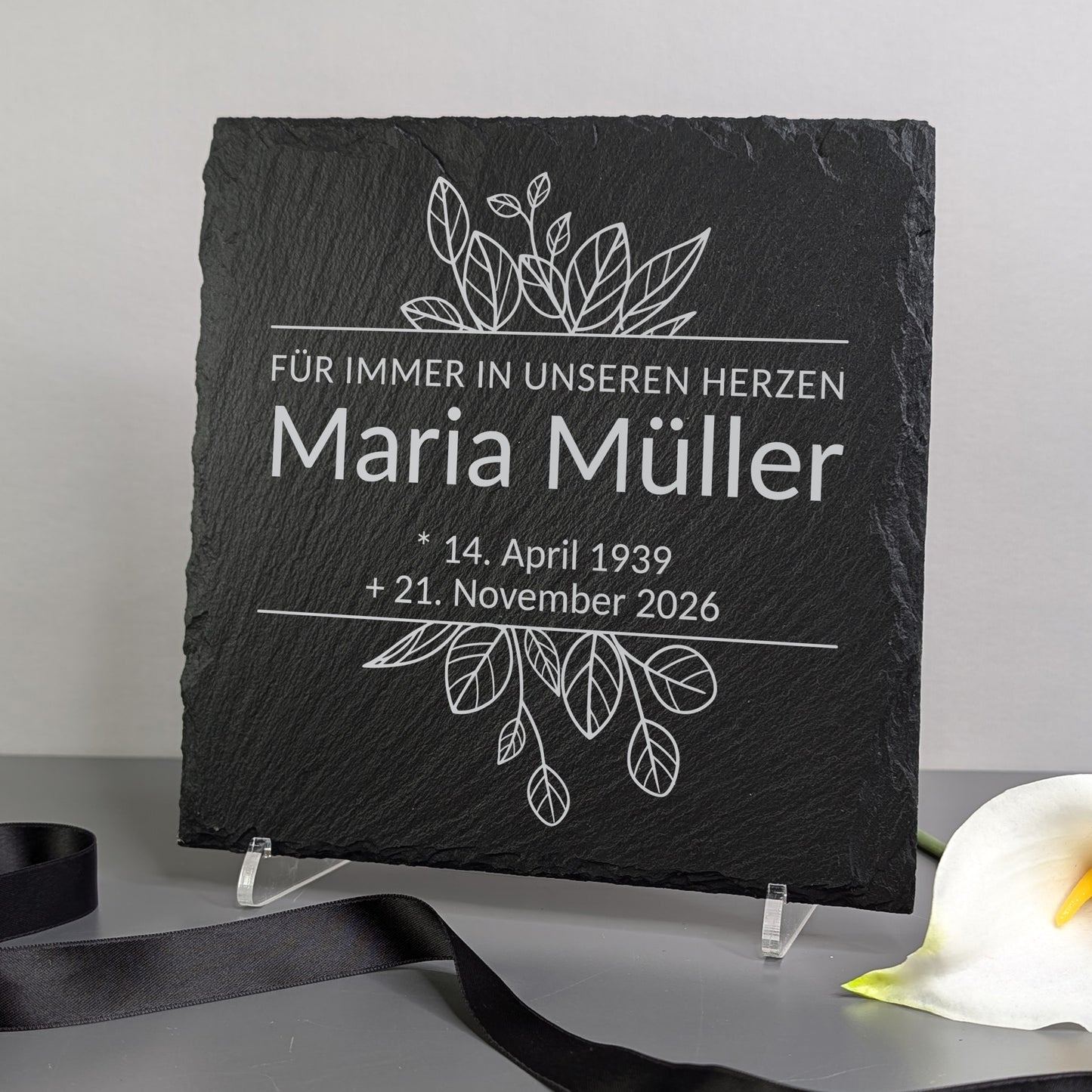Gedenktafel auf einem Ständer dekoriert – neben Blume und Trauerband platziert