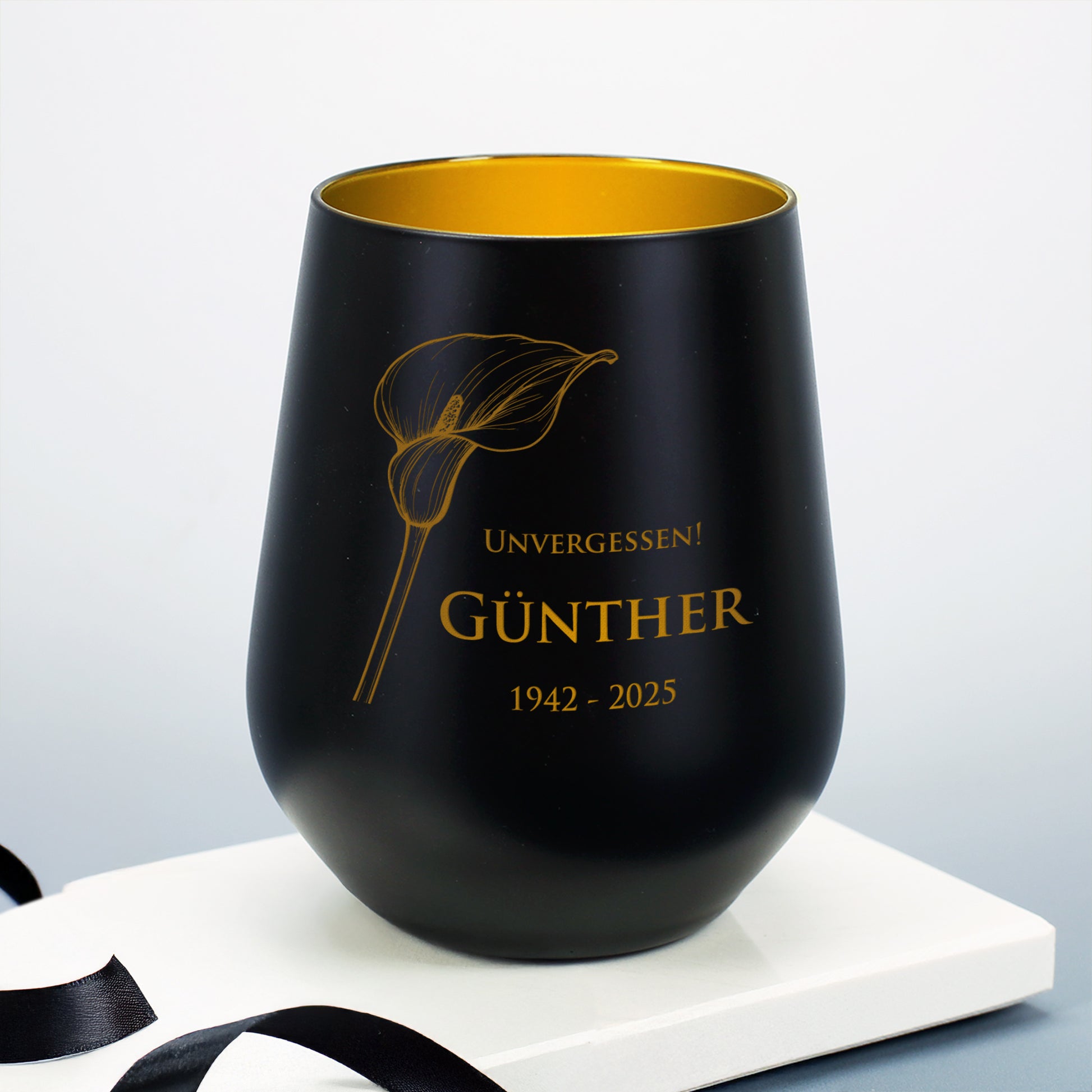 Schwarzes Windlicht mit Calla-Motiv, graviert mit "Unvergessen! Günther 1942–2025", auf weißem Sockel mit Schleifenband