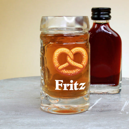 Mini-Schnapsglas mit Brezel-Motiv und Namensaufdruck Fritz, im Hintergrund kleine Schnapsflasche