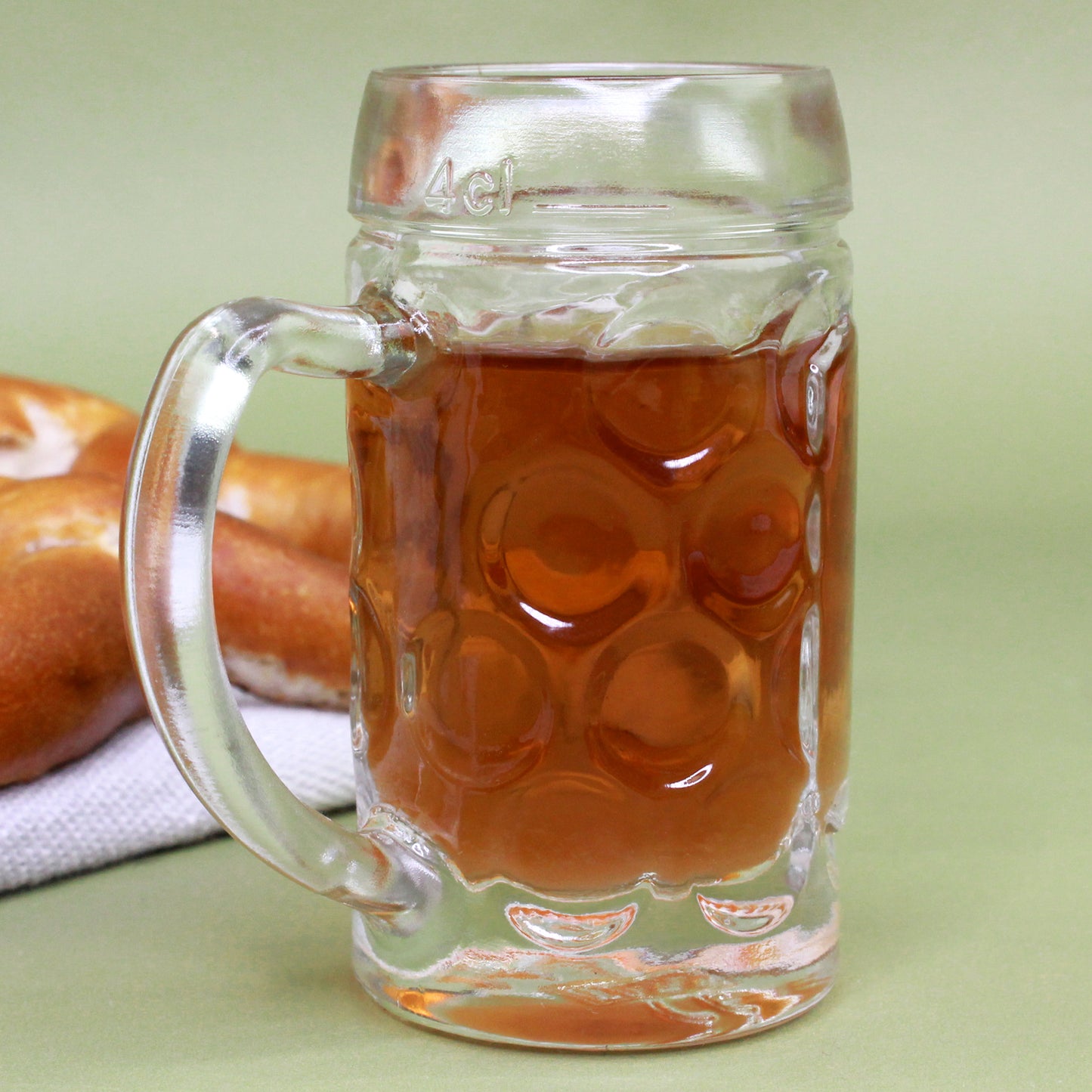 Rückseite des Mini-Bierkrugs mit sichtbarer 4 cl-Füllstrich-Prägung, Henkel links, Brezel im Hintergrund