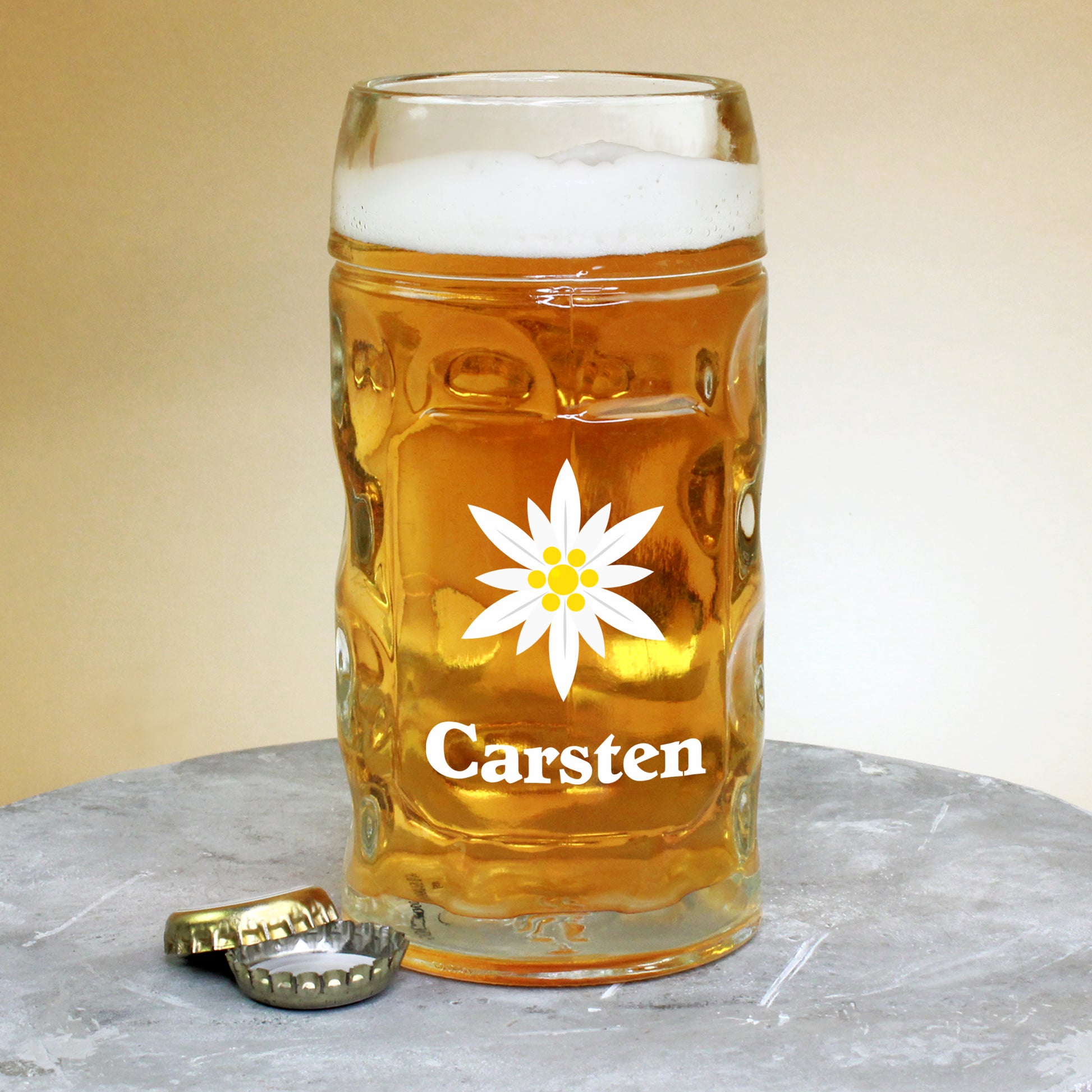 Personalisiertes Bierglas mit Edelweiß-Motiv – Name Carsten und zwei geöffnete Kronkorken auf grauer Platte