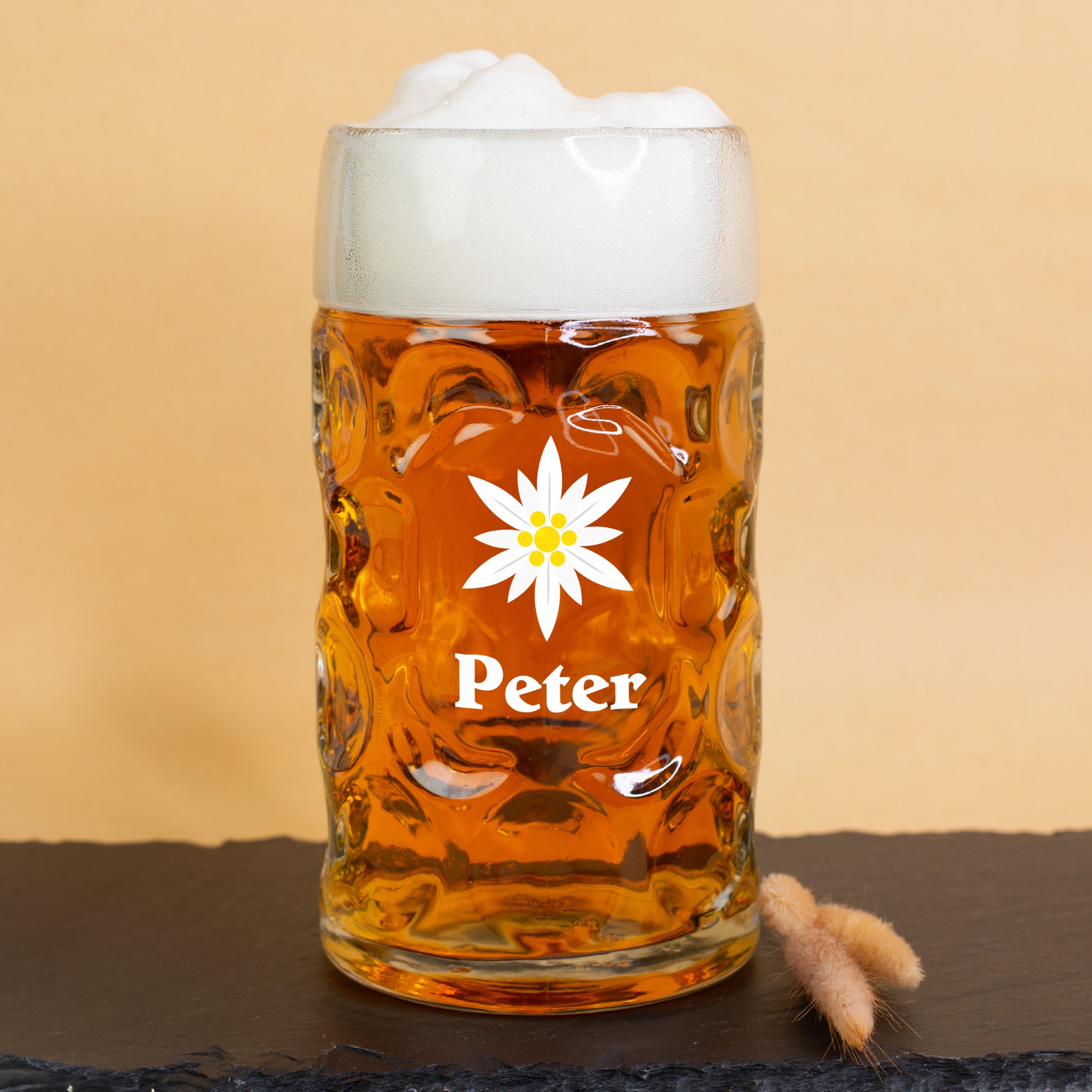 Personalisierter 1-Liter-Bierkrug mit Edelweiß-Motiv und Name Peter – gefüllt mit Bier und Schaumkrone auf Schieferplatte