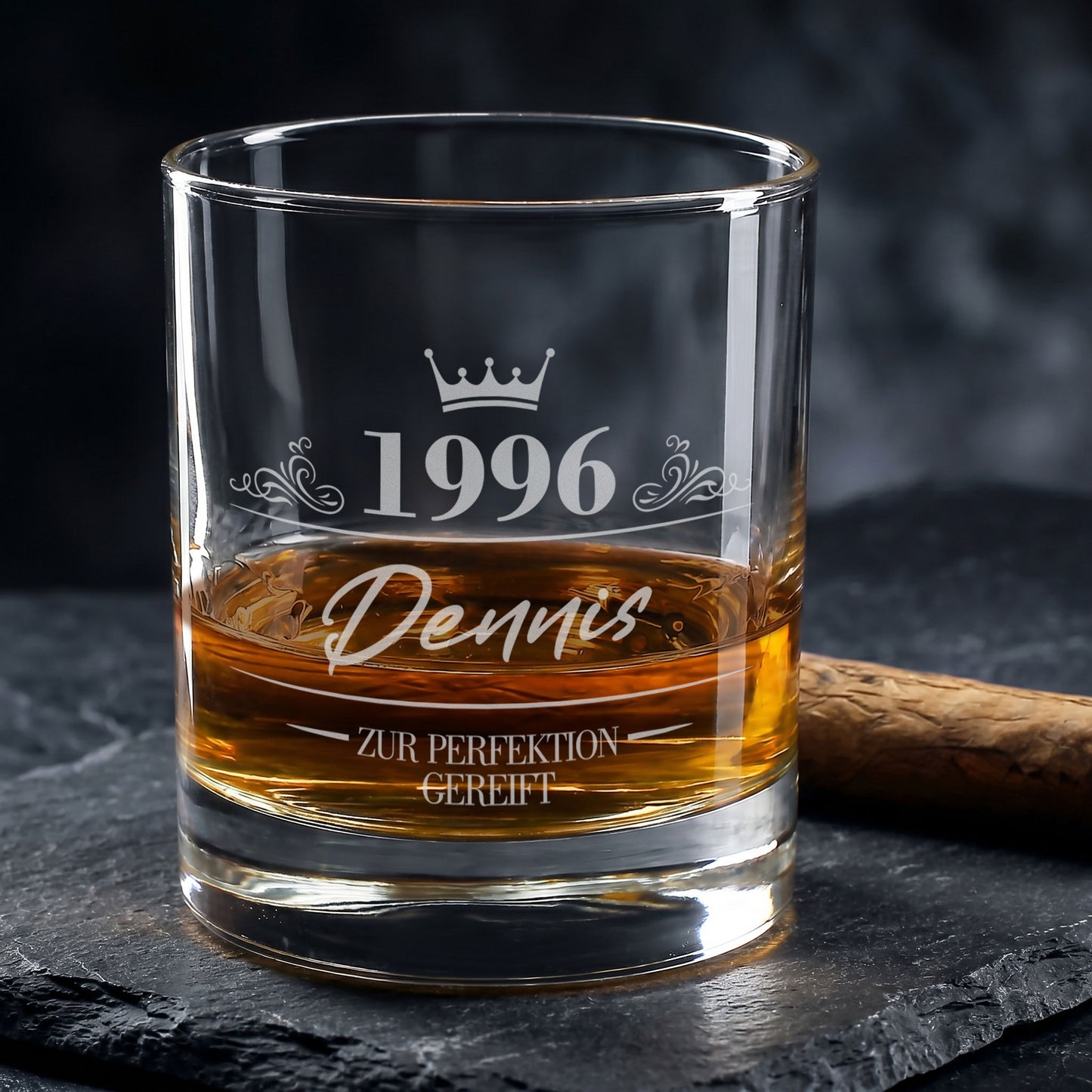 Personalisiertes Whiskyglas zum Geburtstag mit Gravur von 1996, Name Dennis und Krone, gefüllt mit Whisky neben Zigarre