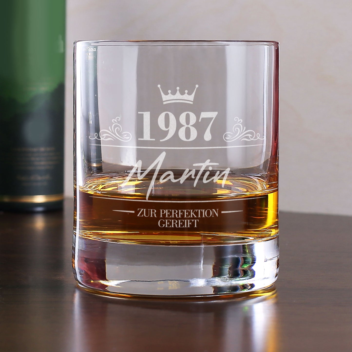 Personalisiertes Whiskyglas mit Gravur von 1987, Name Martin und Krone, gefüllt mit Whisky auf Tisch