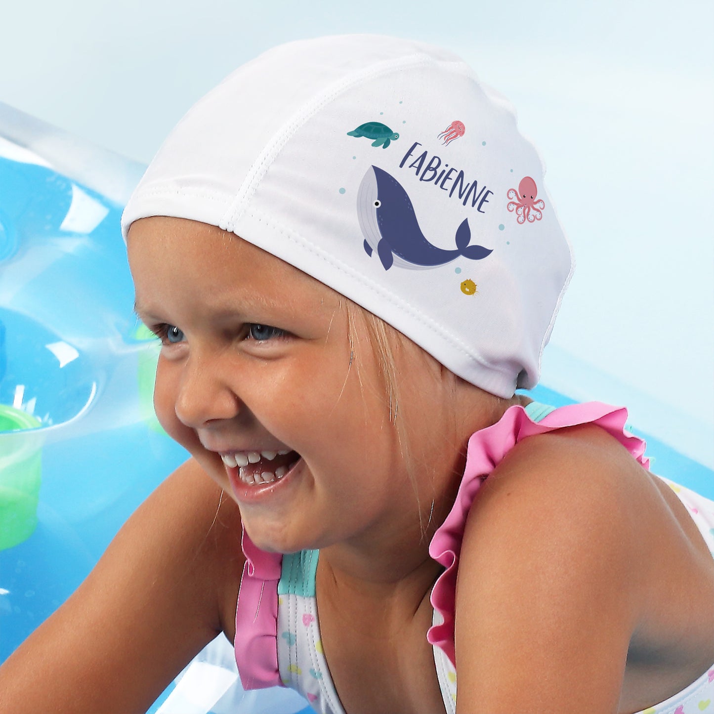 Lächelndes Kind im Wasser mit Badekappe und pinkem Badeanzug