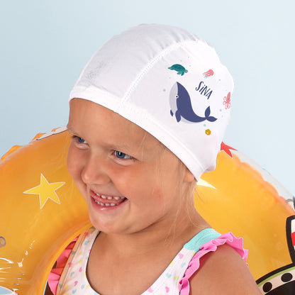 Mädchen mit gelben Schwimmflügeln trägt Badekappe mit Wal-Design