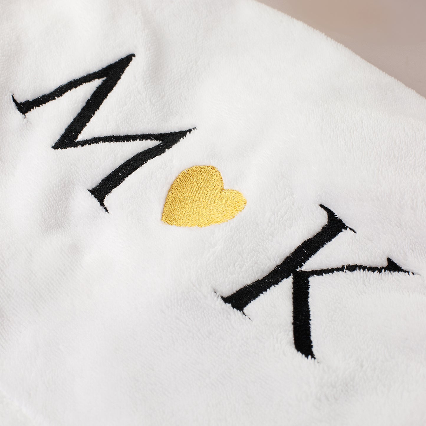 Detailaufnahme Stickerei auf weißem Bademantel mit Buchstaben und goldenem Herz in der Mitte