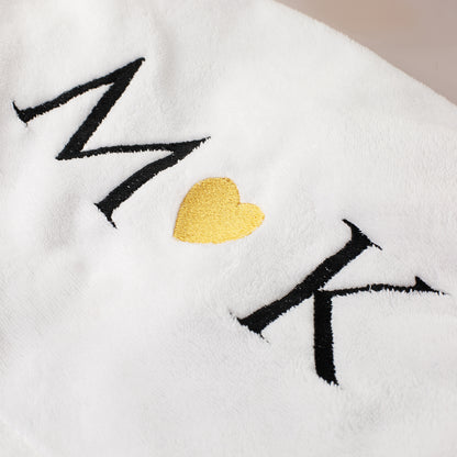 Detailaufnahme Stickerei auf weißem Bademantel mit Buchstaben und goldenem Herz in der Mitte