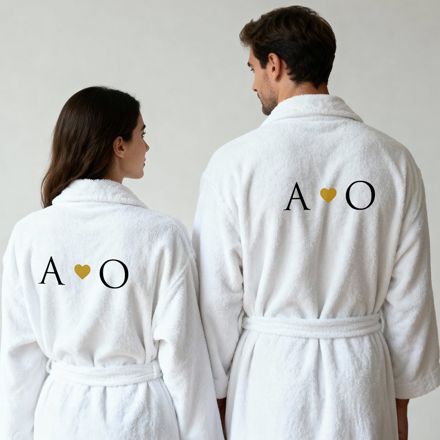 Paar in weißen Bademänteln von hinten, Initialen mit goldenem Herz bestickt, personalisiertes Partner-Set