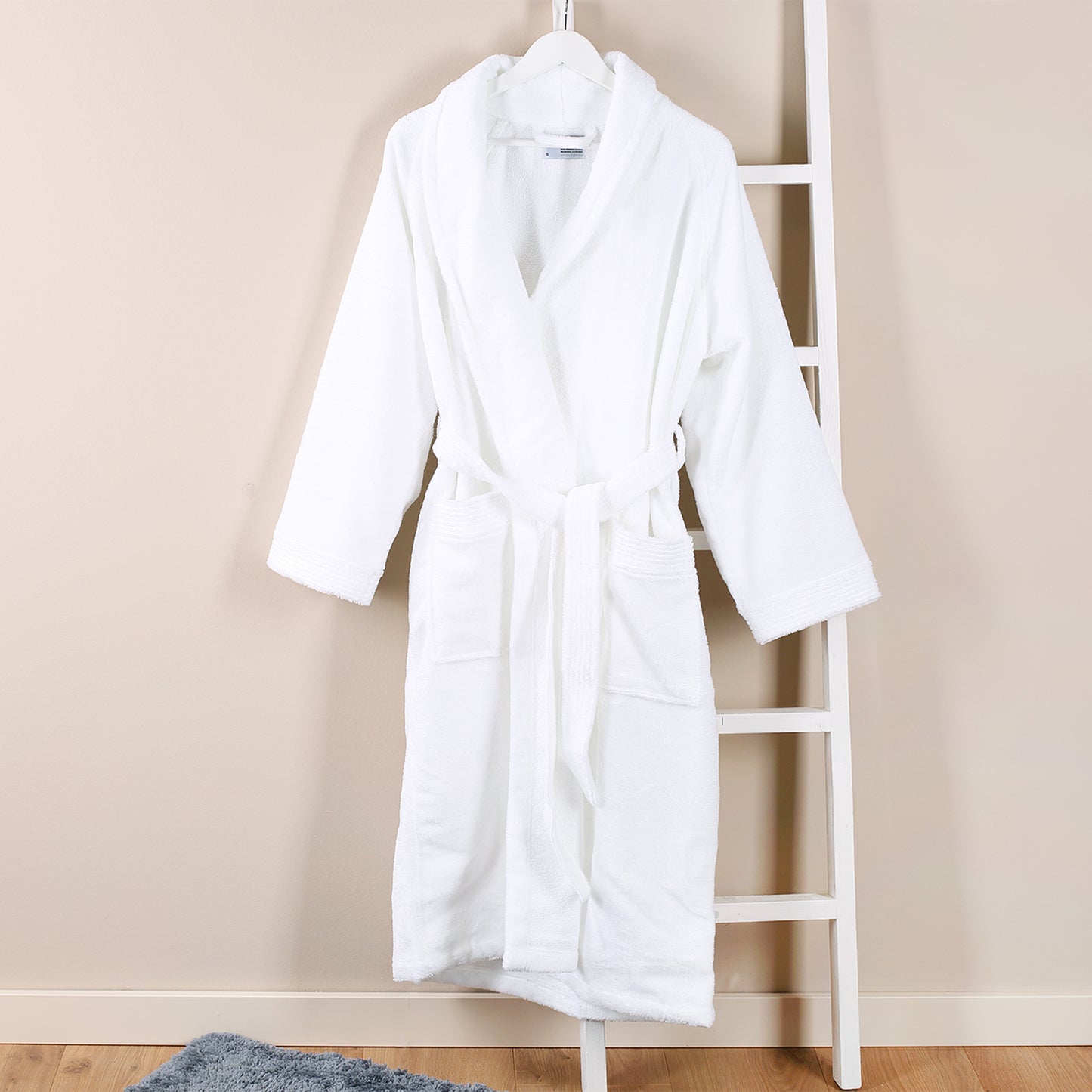 Weißer Bademantel auf einem Bügel aufgehängt, Unisex-Schnitt mit Gürtel und Taschen, Wellness-Look