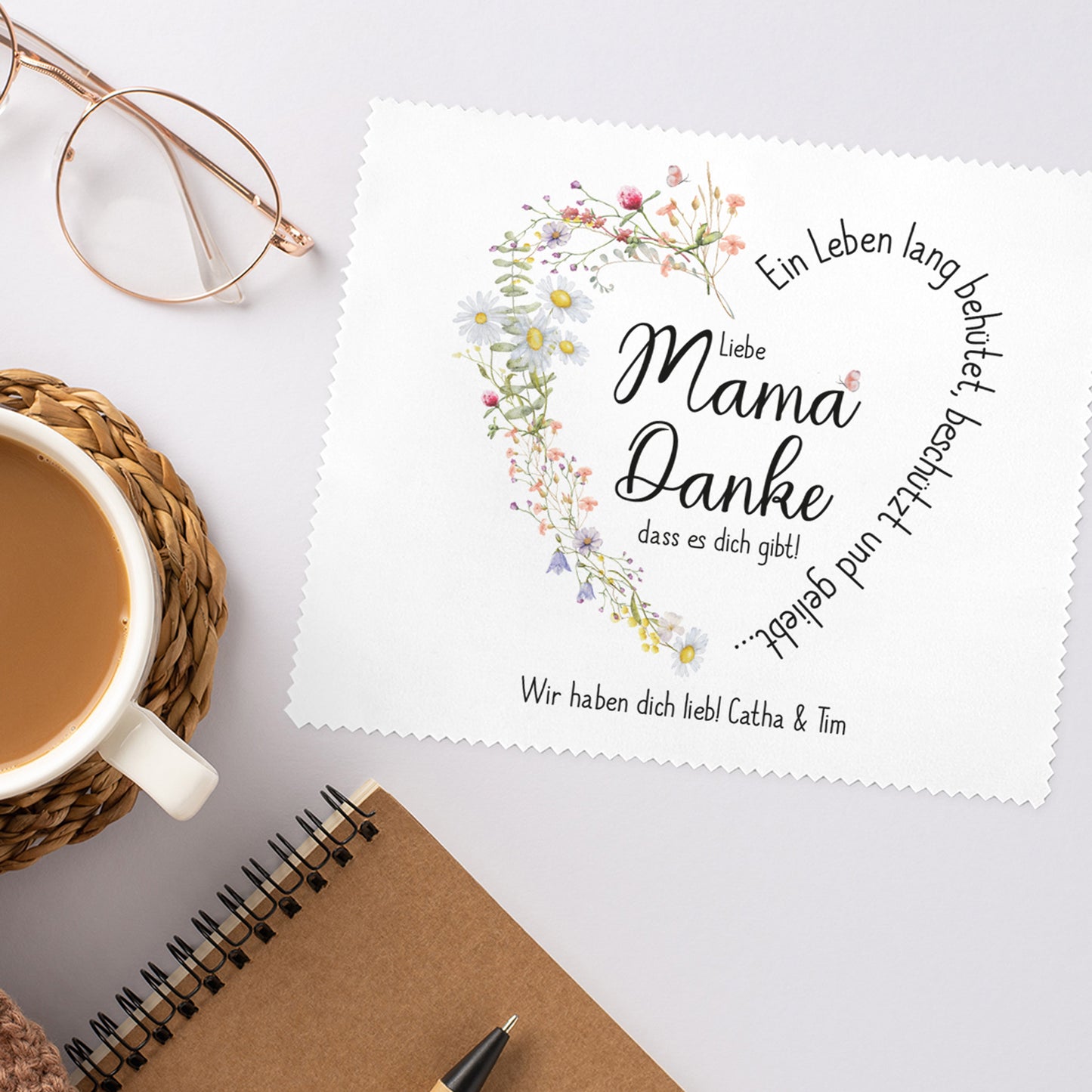 Personalisierbares Brillenputztuch mit floralem Herzmotiv, platziert auf hellem Untergrund mit Brille zur Veranschaulichung der Nutzung.