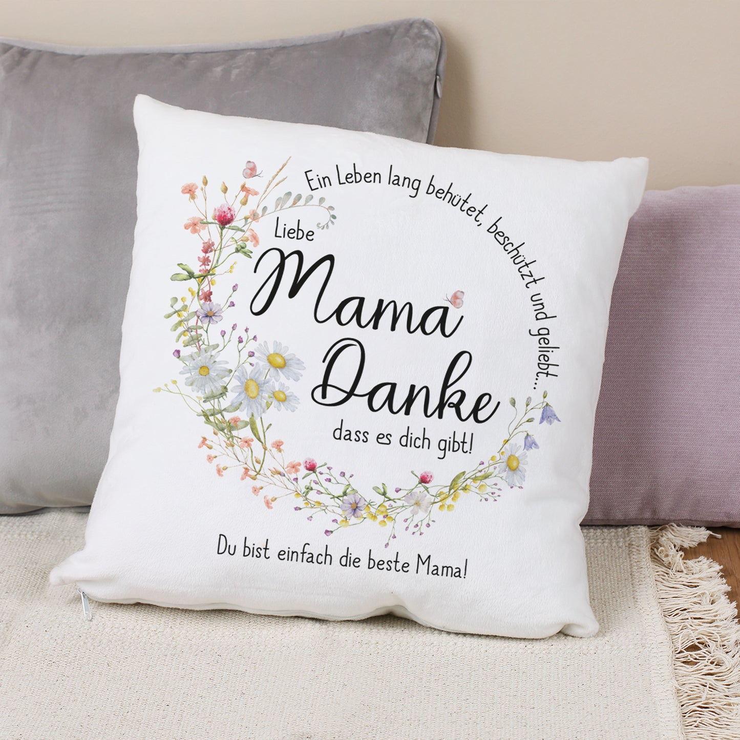 Ein weißes Kissen mit einem liebevollen Muttertagsmotiv. Der Text „Mama Danke, dass es dich gibt!“ ist umgeben von einem zarten Wiesenblumenkranz. Individuelle Personalisierung am unteren Rand.