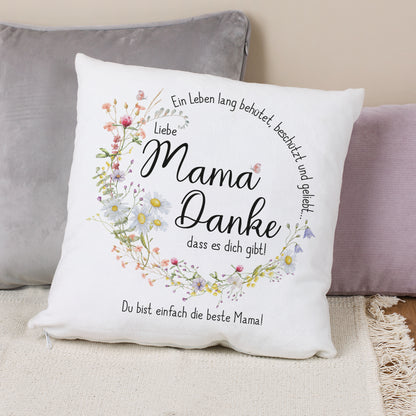 Ein weißes Kissen mit einem liebevollen Muttertagsmotiv. Der Text „Mama Danke, dass es dich gibt!“ ist umgeben von einem zarten Wiesenblumenkranz. Individuelle Personalisierung am unteren Rand.