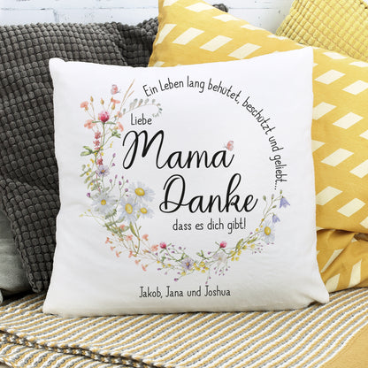 Personalisierbares Kissen mit Muttertagsmotiv auf einer Couch. Wiesenblumen umranden die liebevolle Botschaft für die Mama.