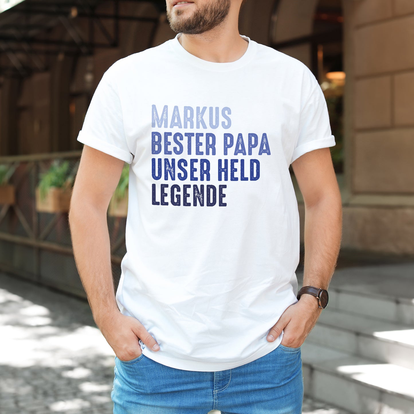 Mann trägt weißes T-Shirt mit Aufdruck „Markus – Bester Papa – Unser Held – Legende“ im Freien