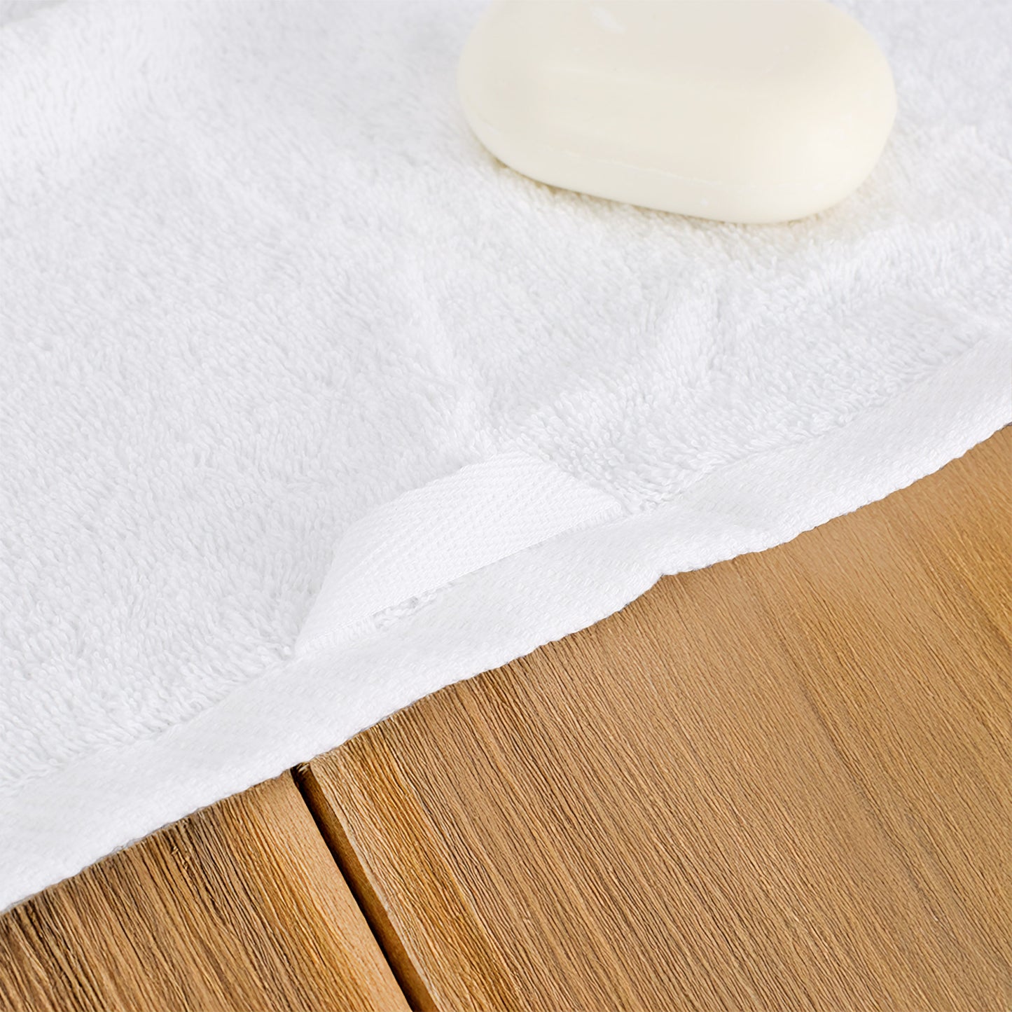 Detailaufnahme von weißem Handtuch aus Baumwolle mit Aufhängeschlaufe und weicher Frottierstruktur auf Holzoberfläche