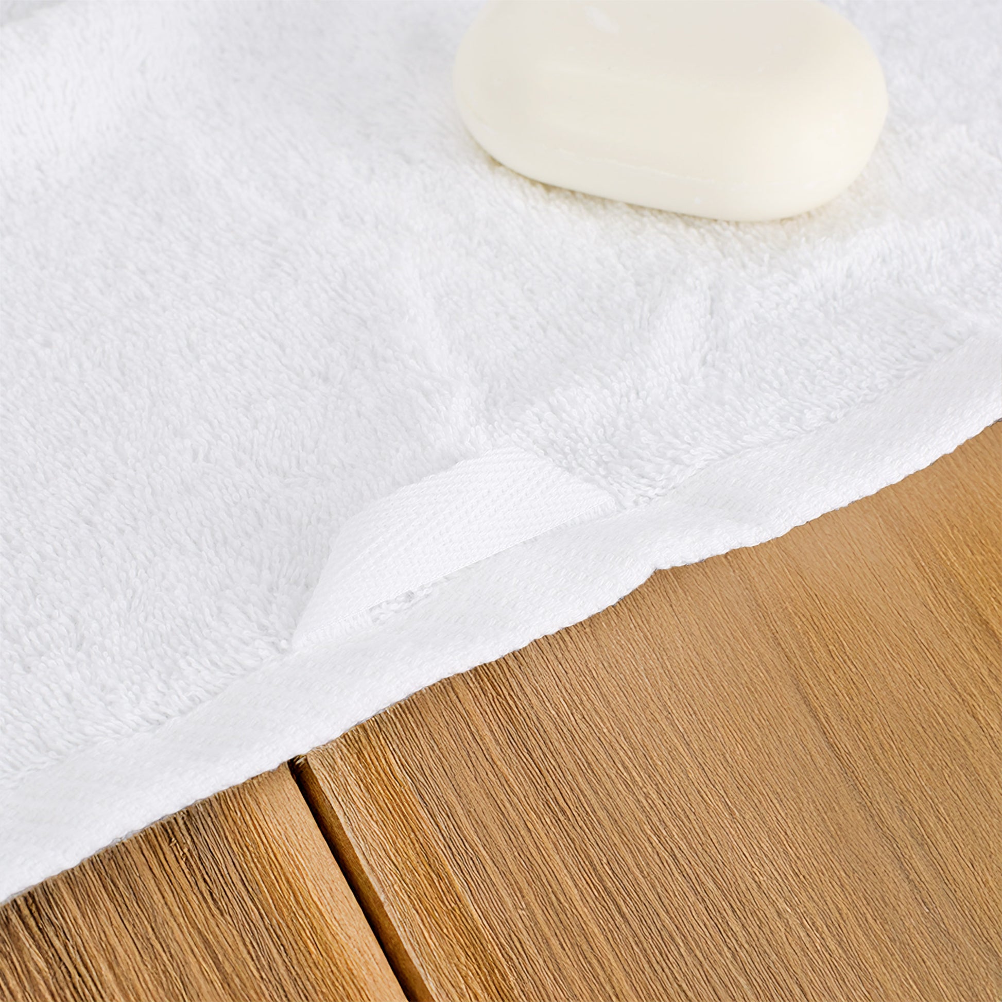 Detailaufnahme von weißem Handtuch aus Baumwolle mit Aufhängeschlaufe und weicher Frottierstruktur auf Holzoberfläche