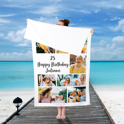 Person steht am Strand und hält ein individuell bedrucktes Badetuch mit Foto und Text von hinten in die Höhe – sommerliche Kulisse mit Meerblick.