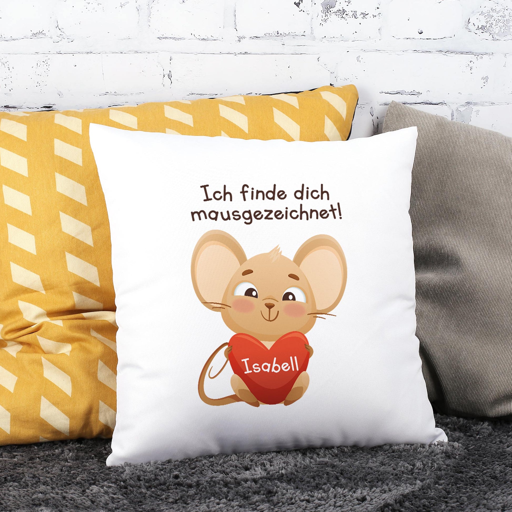 Weißes Dekokissen mit Mausmotiv und personalisiertem Herz mit Name Isabell auf Sofa vor Ziegelwand