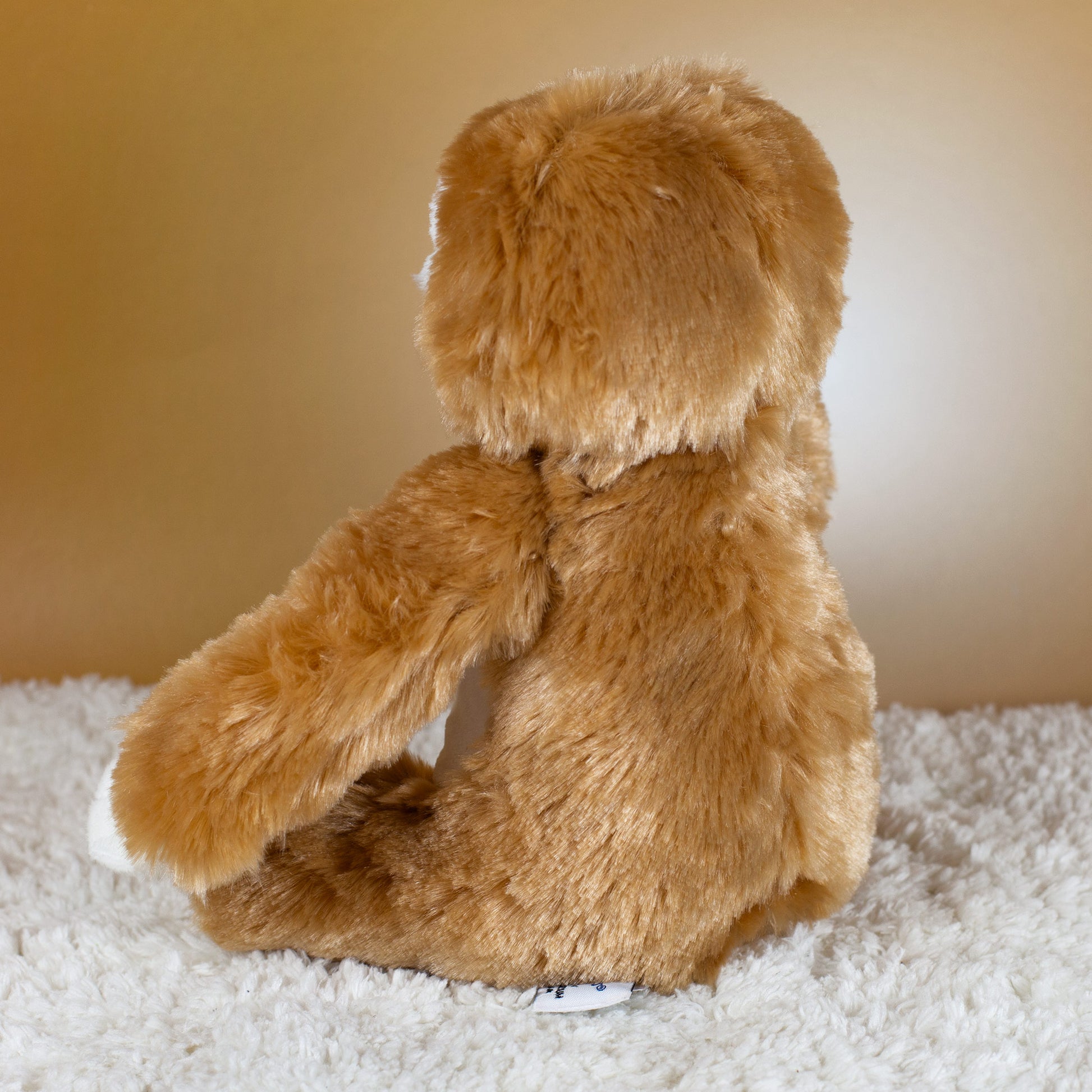 Rückansicht des braunen Kuscheltiers Faultier mit weichem Plüschfell auf hellem Untergrund.