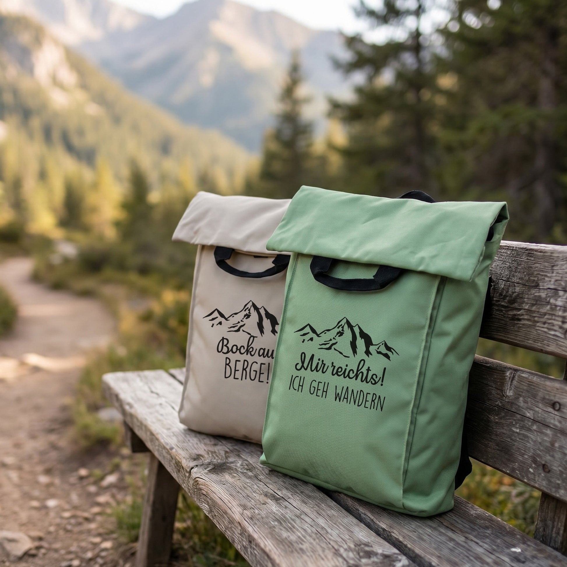 Zwei personalisierte Rucksäcke mit Bergmotiv in Beige und Jadegrün auf einer Holzbank in Berglandschaft