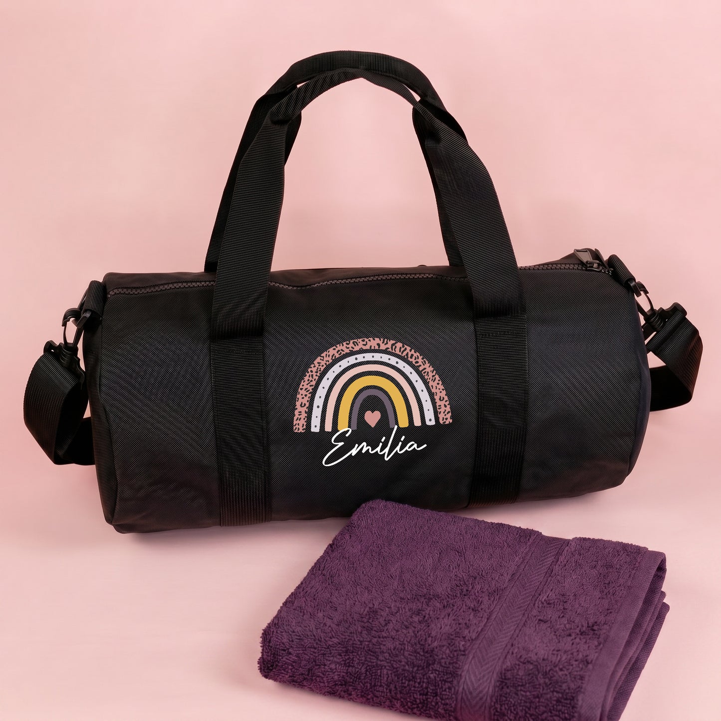 Personalisierte schwarze Sporttasche mit Regenbogen Motiv und Name Emilia neben lila Handtuch