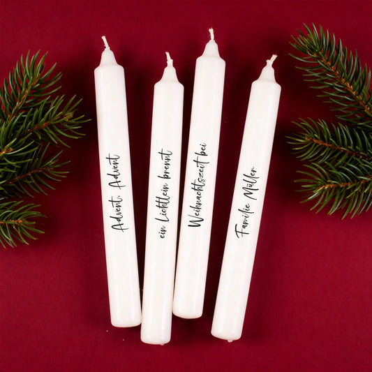 Vier personalisierte Adventskerzen mit schwarzer Schrift auf rotem Hintergrund und Tannenzweigen.